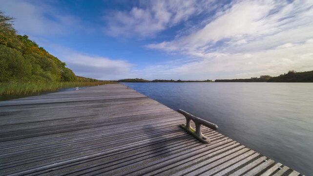 Time lapse of a timber lake pier in the foreground and castle ruin island with forest in distance on a cloudy sunny day at Lough Key in county Roscommon in Ireland.