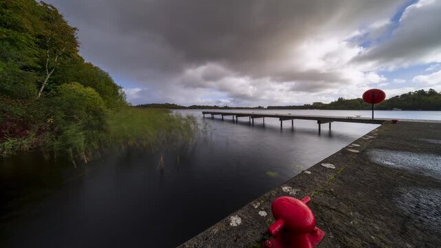 Time lapse of a timber lake pier in the foreground and castle ruin island with forest in distance on a cloudy sunny day at Lough Key in county Roscommon in Ireland.