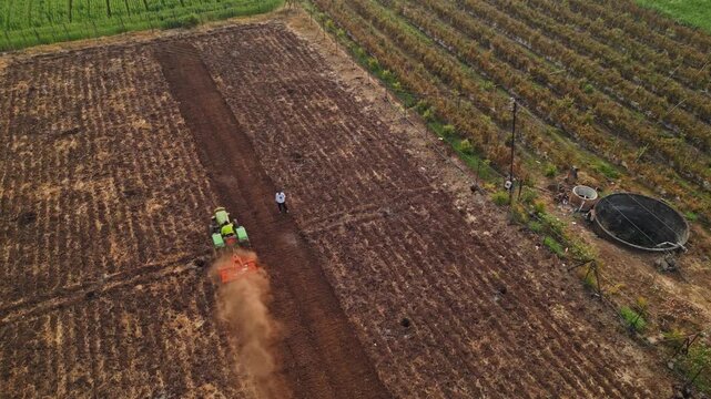 Aerial view of lush Adgaon, Nashik farmland during harvest, golden crops swaying, farmers at work, tractors in motion, showcasing vibrant rural life and agricultural abundance from above