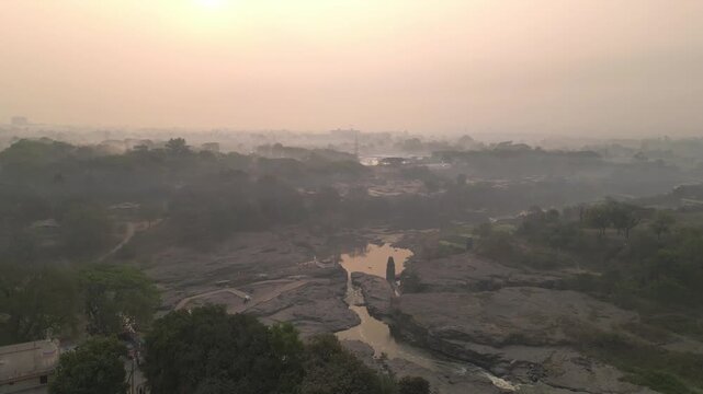 Aerial view of Nashik at evening, golden sunlight reflecting off the Godavari River, city streets winding below, hills framing the skyline, capturing the serene yet bustling urban riverside charm