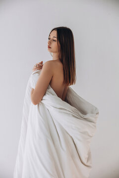 Beauty portrait of a model, a beautiful brunette girl with straight long hair dressed in a long white blanket on a white background