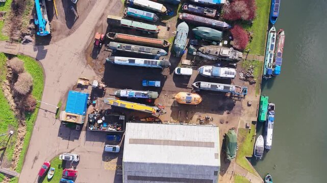 Top-down drone over Stanstead Abbots marina in Hertfordshire, UK, flying forward above main building and boats on hardstanding, with River Lea to the right in daylight.