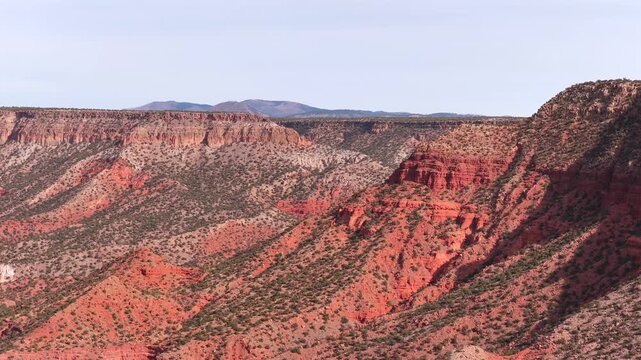 A sweeping drone perspective captures the monumental scale of crimson sandstone ridges and a vast mountain horizon. This 4K vista provides a majestic background for cinematic world building.