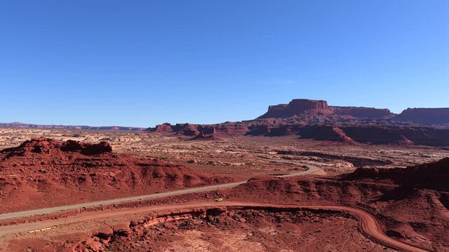 Drone descent reveals a solitary vehicle parked on a remote desert road. The massive sandstone buttes and clear blue horizon create a sense of scale for this location agnostic alien landscape.