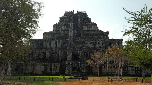 Slow pull-back from Koh Ker pyramid temple facade framed by trees and grass in Siem Reap
