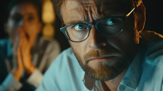 An intense scene from a movie or show, featuring a man wearing glasses with a concerned facial expression.