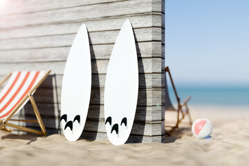 Two white surfboards standing upright on a sandy beach beside a lounge chair and a wooden structure, with a ball nearby © cozzdesign