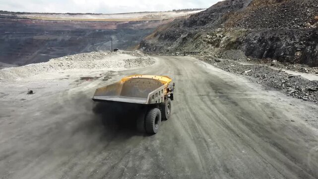Yellow haul trucks travel along a dirt road in a deep open pit mine