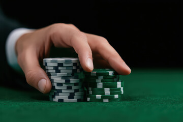 Poker chip stack green and black with hand on green felt table close up side angle view of professional poker game risk and strategy concept