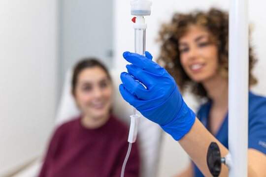 Close Up of Doctor Hand Adjusting IV Drip, Medical Procedure, Healthcare Concept. Professional medical worker in blue gloves holding intravenous infusion equipment with blurred patient background.