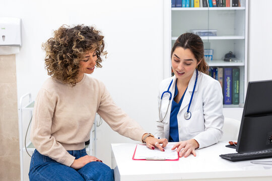 Friendly female physician pointing at medical report on clipboard during consultation with patient. Doctor explaining test results to woman in office. Healthcare and medicine professional insurance.