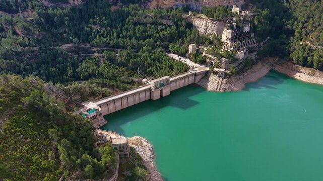 Aerial view of Benageber Dam on the Turia River, showing concrete gravity dam, intake structure, and vivid reservoir surrounded by forested mountains
