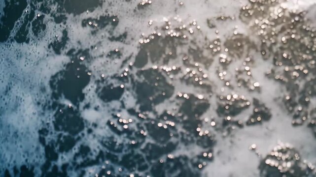 Ocean waves breaking on sandy shore, white foam creating intricate patterns and sparkling water that suggest calm movement, coastal texture and serene seaside beauty