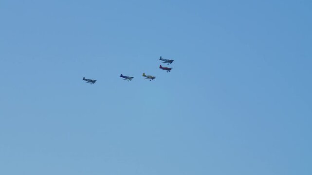 A group of propeller-driven light aircraft is flying in the sky. A squadron of five vintage tourist planes flies in the blue sky.