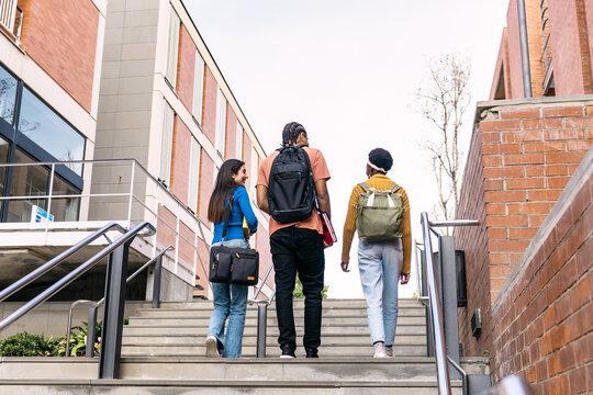 Group of multi ethnic students with backpacks and books ascending university stairs, looking towards a bright future and education