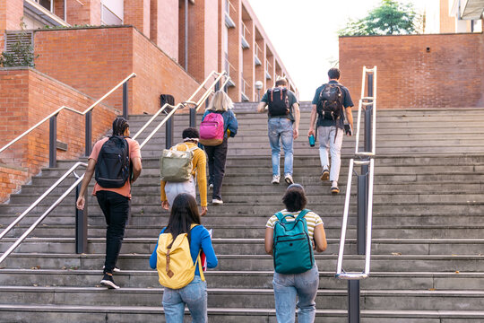 Diverse young students with backpacks walking up outdoor stairs on a university campus, representing education and progress