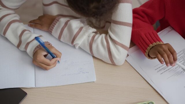 High angle shot of unrecognizable African American sister and brother doing homework at table. Boy doing grammar exercise while girl solving math problem