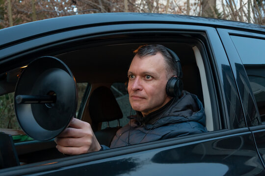 An undercover observer records sound with a directional microphone while monitoring a target from a parked vehicle.