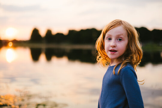 Red haired girl near sunset on lake outside with golden light