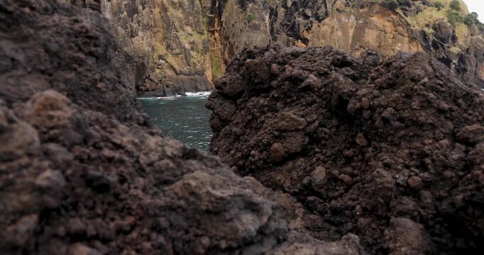 Steep volcanic cliffs by the Atlantic ocean rising from blue water at Capelas, Azores.