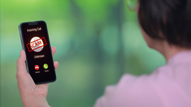 Anxious elder woman holding smartphone looking at screen showing phone scam warning call alert against green nature blur background