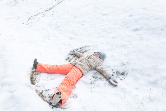 Child enjoying winter making a snow angel outdoors in vibrant clothing