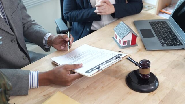 Lawyers reviewing a contract with a house model and gavel on the desk, representing real estate legal consultation, property agreement, and home ownership documentation.