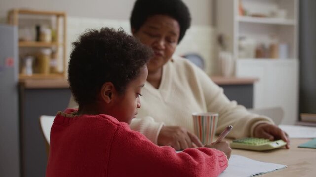 Curly haired African American boy solving math problem while his grandmother supporting him, patting his head