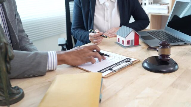 Lawyers reviewing a contract with a house model and gavel on the desk, representing real estate legal consultation, property agreement, and home ownership documentation.