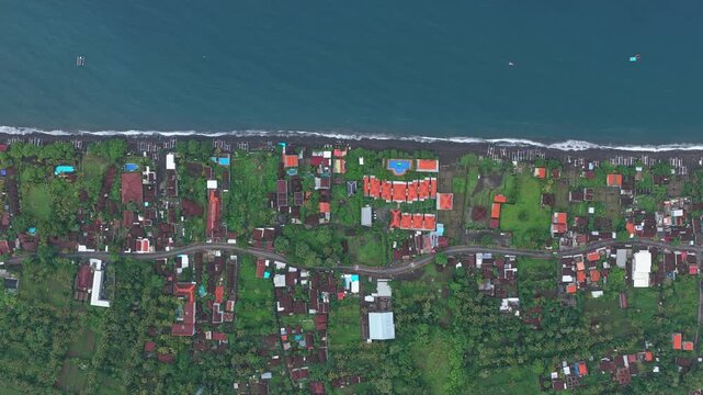 Aerial top down perspective of the coastal village of amed in bali, indonesia. A stunning view of the black sand beach and lush greenery
