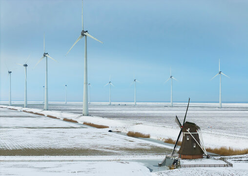 Classic windmill and wind turbines in snowy Eemshaven landscape
