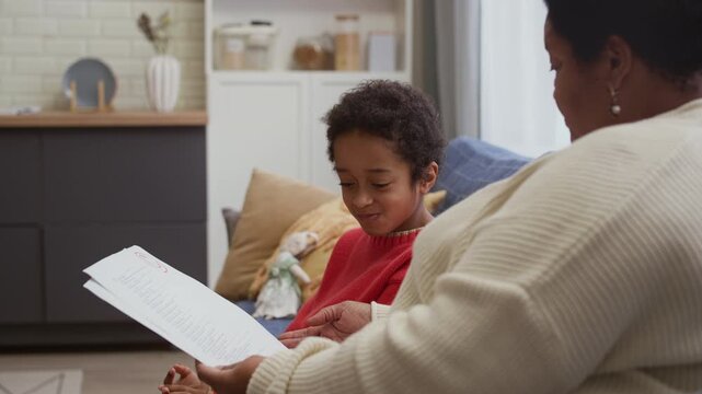 Over shoulder view of African American schoolboy smiling and communicating with grandparent who checking his test grade