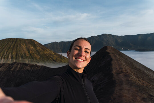 Smiling traveler taking selfie on volcano crater in Java Indonesia