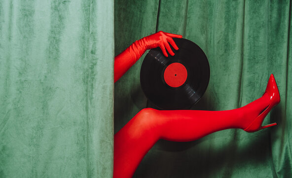 Red gloved hand and leg with vinyl record and high heel by green velvet curtain