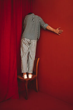 Person in striped clothing standing on chair in red corner expressing despair
