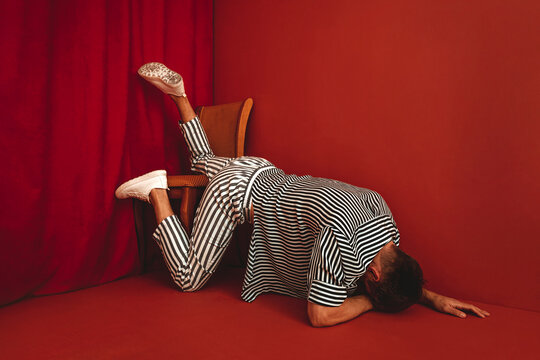 Person in striped clothing lying face down in despair against red wall