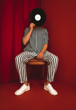 Person in striped outfit holding vinyl record in front of face against red background