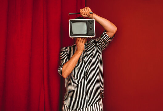 Person with retro television as head in red room with striped shirt