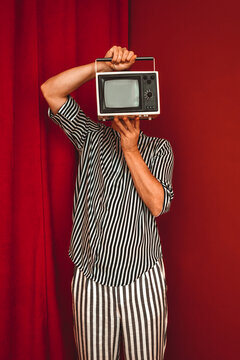Person in striped clothing holding retro TV in front of face in red room