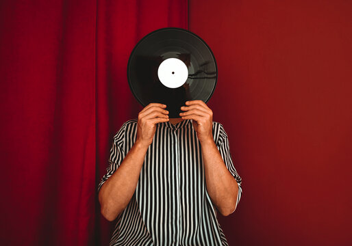 Person in striped shirt holding vinyl record in front of face indoors