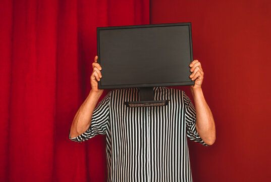 Person in striped shirt holding monitor in front of face against red background