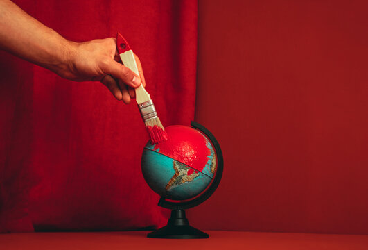 Hand painting globe red with brush symbolizing conflict and change