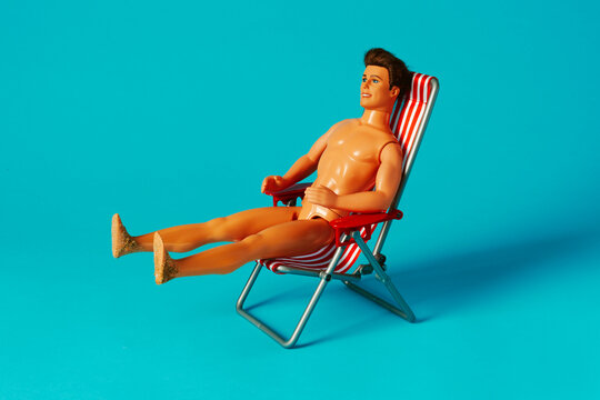 Nude male beach doll with sandy feet on striped deck chair in turquoise studio