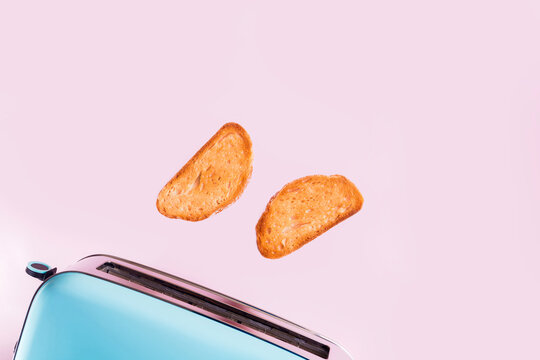 Toasted bread slices popping from blue retro toaster on pink background
