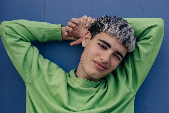 Portrait of playful young adult relaxing with hands behind head outdoors
