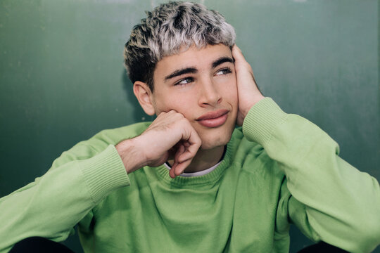 Thoughtful young man resting outdoors with head on hand in green sweater