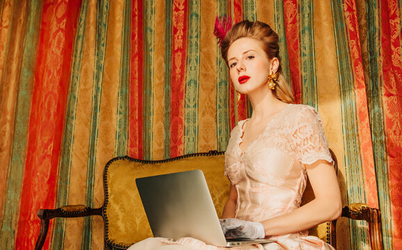 Woman in vintage dress using laptop on retro sofa in elegant interior