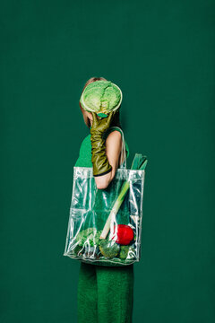 Fashionable woman with vegetable bag and green gloves in front of green backdrop