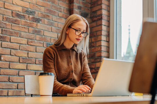 Woman in brown sweater working on laptop at modern office desk