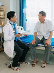 Obraz premium An Asian male doctor and an elderly patient are talking on a bed in a hospital room.